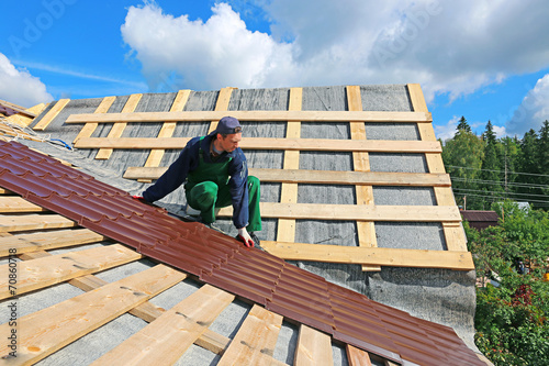 Worker puts the metal tiles on the roof