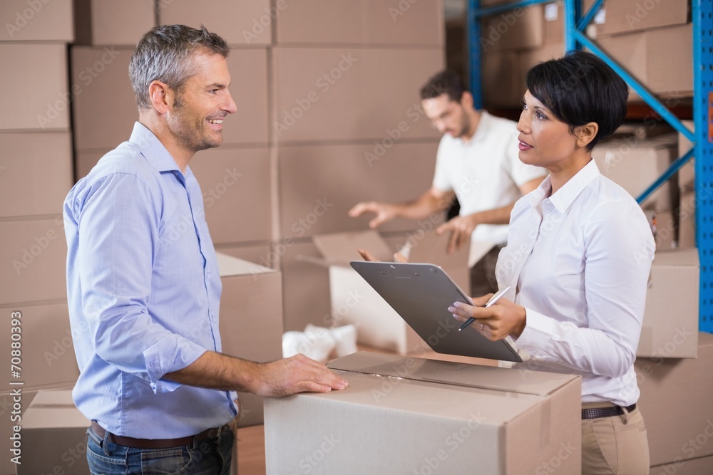 Warehouse manager writing on clipboard talking to colleague Warehouse manager writing on clipboard talking to colleague