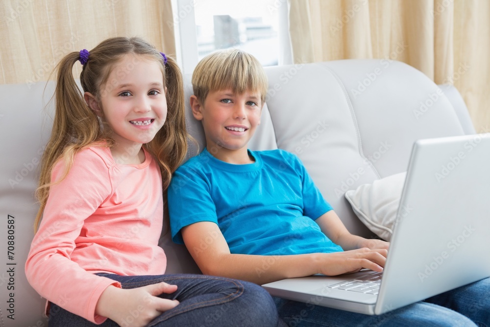 Happy siblings using laptop on sofa Happy siblings using laptop on sofa