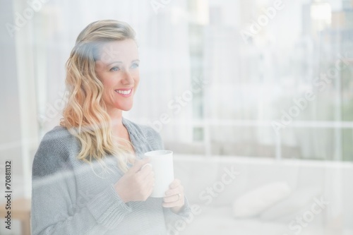 Smiling blonde woman holding mug of coffee looking away
