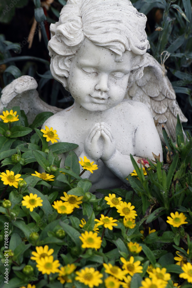 little praying angelic figure among the growing flowers on tomb