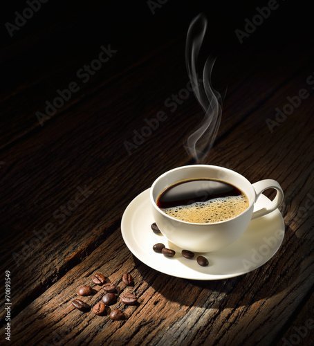 Cup of coffee with smoke and coffee beans on old wooden table