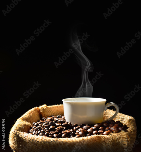 Cup of coffee with smoke and coffee beans in burlap sack