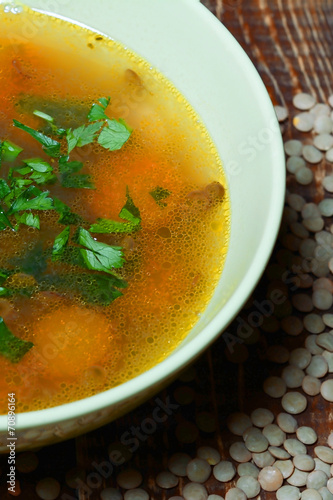 Lentil soup in a green bowl on old table.