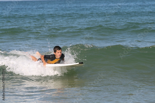 un garçon jeune adolescent fait du surf sur sa planche dans l'océan en combinaison de surfeur