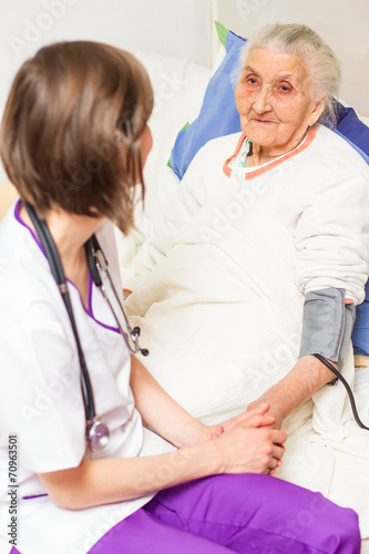 young nurse caregiving an old lady lying in bed