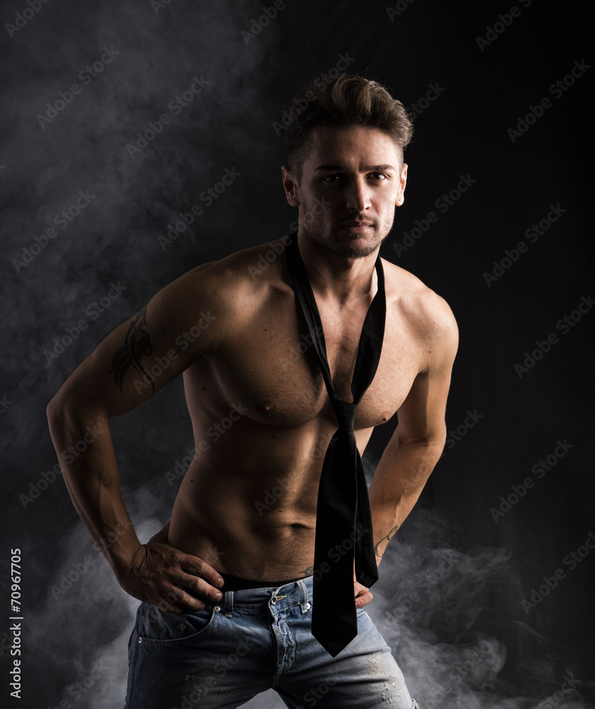 Handsome shirtless muscular man standing on dark background