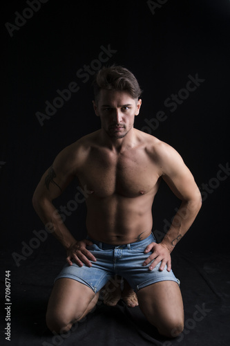 Handsome shirtless muscular man on his knees on dark