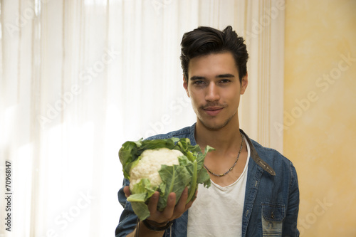 Smiling young man holding a fresh cauliflower in his hand
