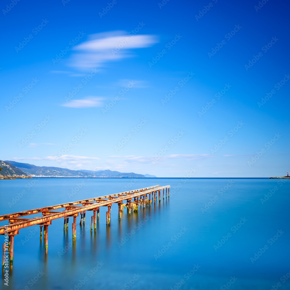 Wooden pier or jetty remains on a blue ocean lake. Long Exposure