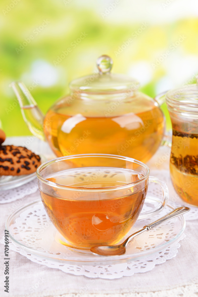 Teapot and cups of tea on table on bright background