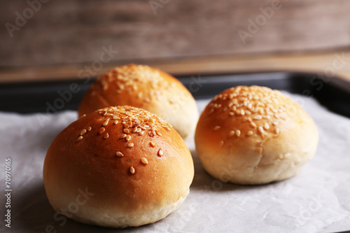 Tasty buns with sesame on oven-tray, on wooden background