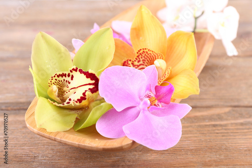 Tropical orchid flowers in bowl on wooden background