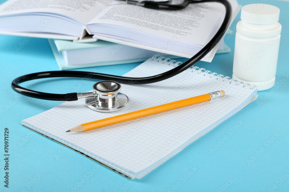 Medical stethoscope with notepad and books on blue background Medical stethoscope with notepad and books on blue background