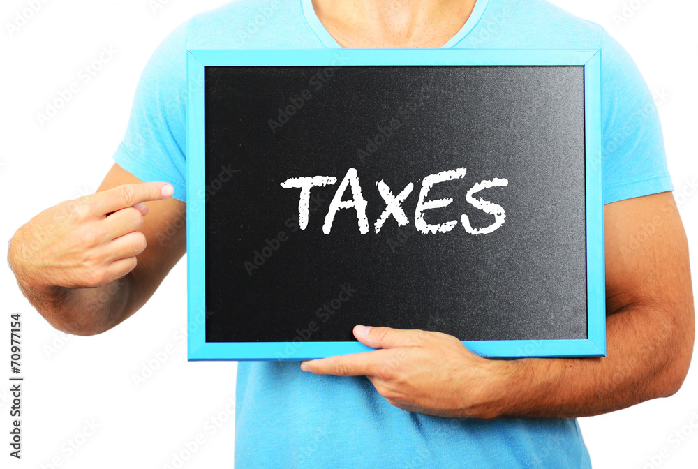 Man holding blackboard in hands and pointing the word TAXES Man holding blackboard in hands and pointing the word TAXES