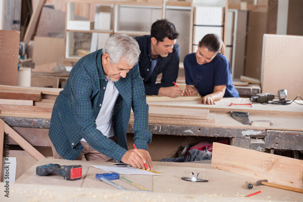 Architect Working On Blueprint With Coworkers In Background Architect Working On Blueprint With Coworkers In Background
