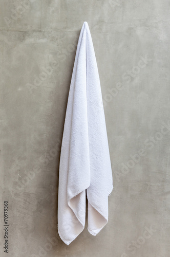 The white towel is hanging on a hanger with concrete wall in the