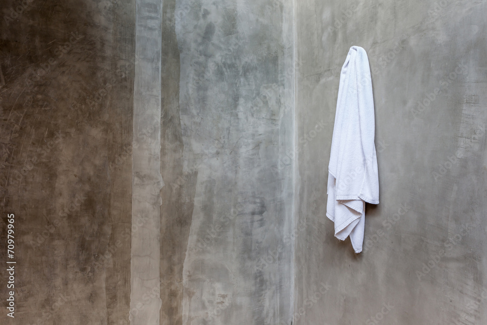 Naklejka premium Hanging white towel draped on exposed concrete wall in the bathr