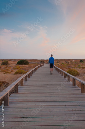 Man walking by a wooden footbridge. Dunes, Algarve, Portugal