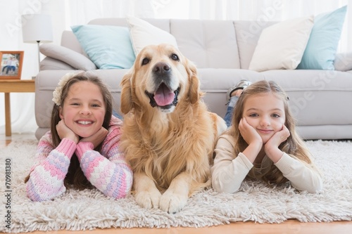 Sisters lying on rug with golden retriever smiling at camera