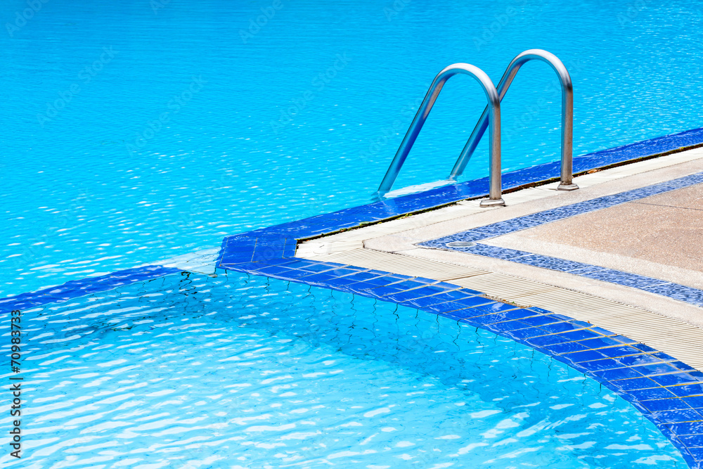 A view of curved light clear blue swimming pool with steel ladde