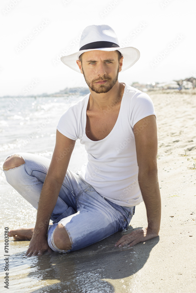 Man on beach sit in sand wearing hipster summer hat.