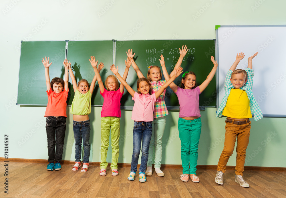 Obraz premium Kids stand with arms up in line near blackboard