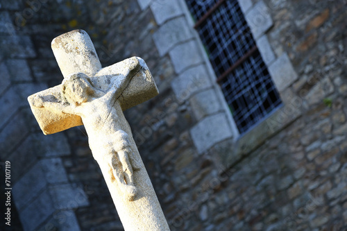 Closeup to stone cross statue in front of an old building photo