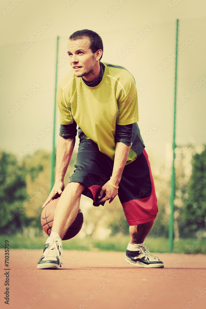 Young man on basketball court dribbling with ball. Vintage mood