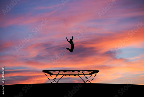 silhouetted man jumping on trampoline in sunset