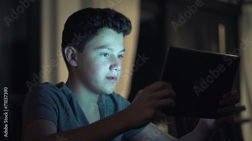Young teenager playing game on tablet computer at night