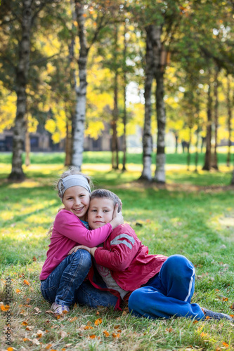 Laughing children embracing on the grass in the autumn park