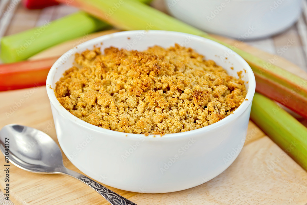Crumble with rhubarb in bowl on tablecloth and board Crumble with rhubarb in bowl on tablecloth and board