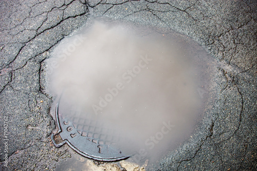 Photo The puddle on the manhole in asphalt surface