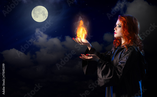 Witch with flame on night sky background