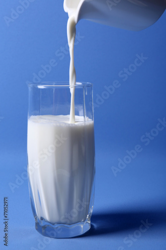 Pours milk in glass on blue background