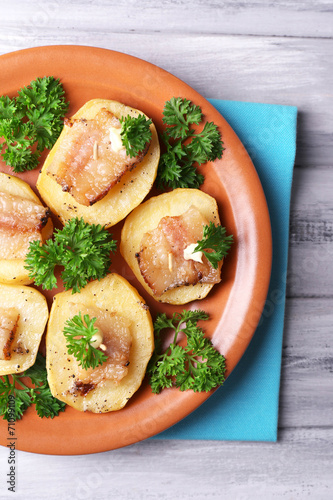 Baked potato with bacon on plate, on wooden background