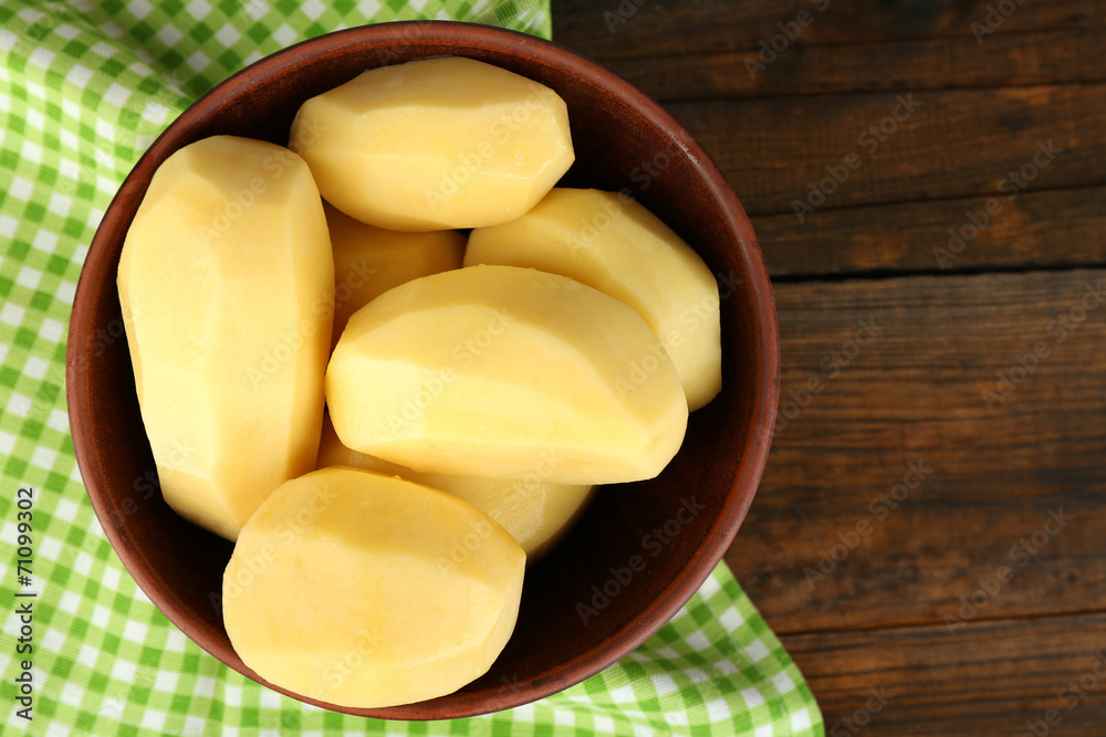 Raw peeled potatoes in bowl  on wooden background