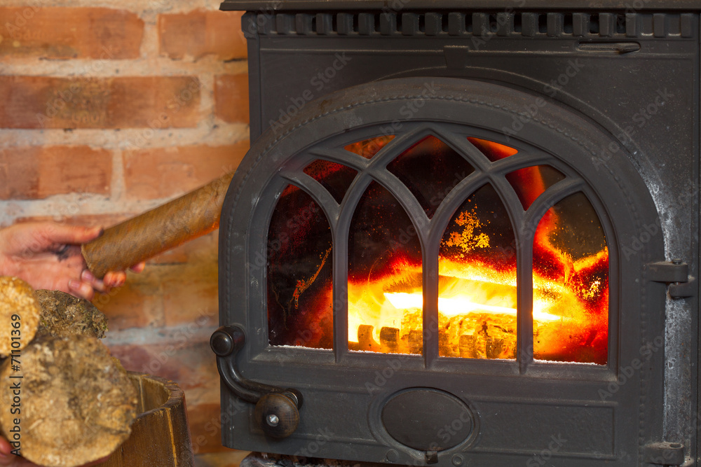 Obraz premium Hand putting wood on fire fireplace. Heating.