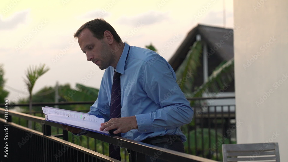Businessman reading documents on the terrace in the evening Businessman reading documents on the terrace in the evening