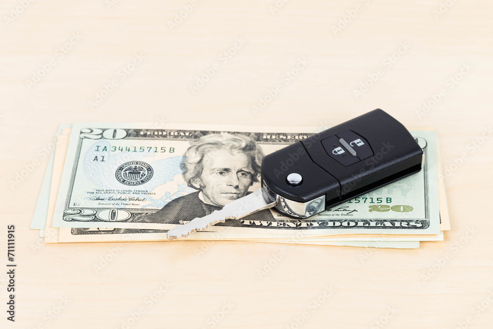 Modern car key and dollar banknote on wooden background Modern car key and dollar banknote on wooden background