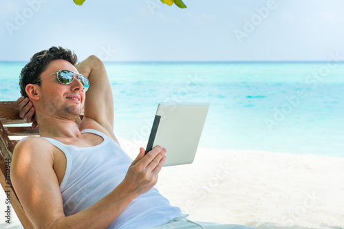 Man relaxing at the beach with tablet, laptop. Maldives island