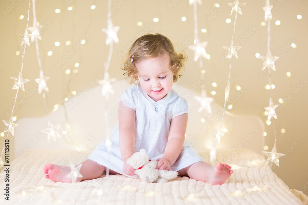 Sweet toddler girl playing with toy between Christmas lights