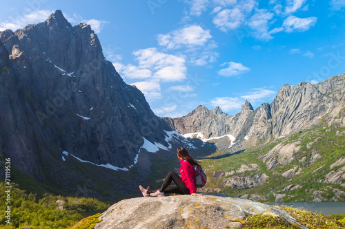 Young tourist woman is sitting on stone near mountain lake