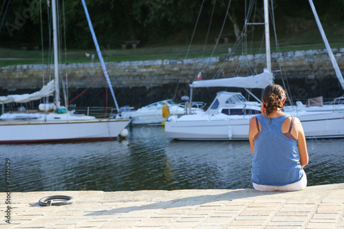 A young woman sitting at the harbor and talking on her phone © GoodPics