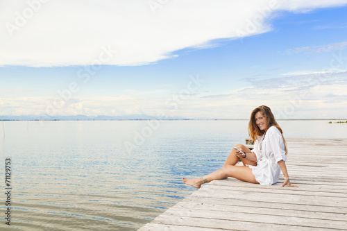 Smiling beautiful young woman sitting on a pier and using a mobi