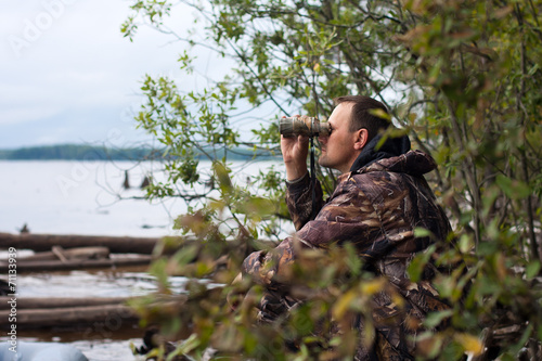hunter looking through binoculars on the river