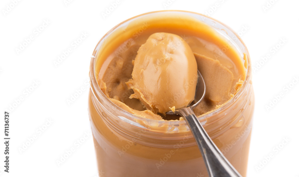 An opened jar of peanut butter with a small spoon An opened jar of peanut butter with a small spoon