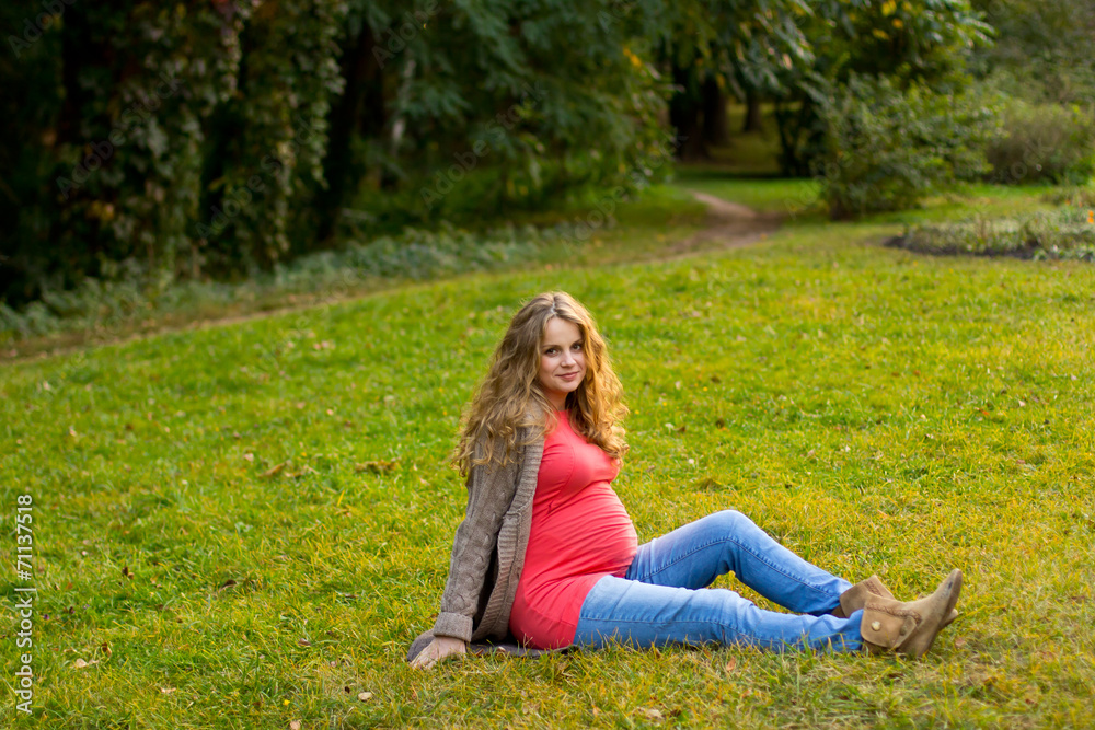 Beautiful pregnant blonde lying on green grass