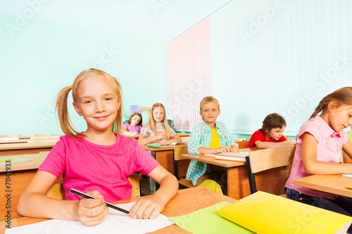 Children write in exercise books and sit at tables